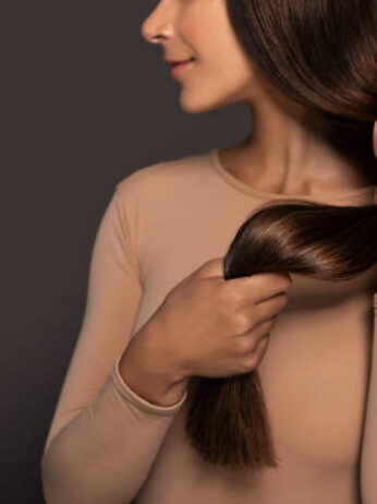 Brunette girl with long straight and shiny hair. Beauty skin woman holding her strong and healthy hair in her hands over grey background. Cosmetic hair beauty salon concept.